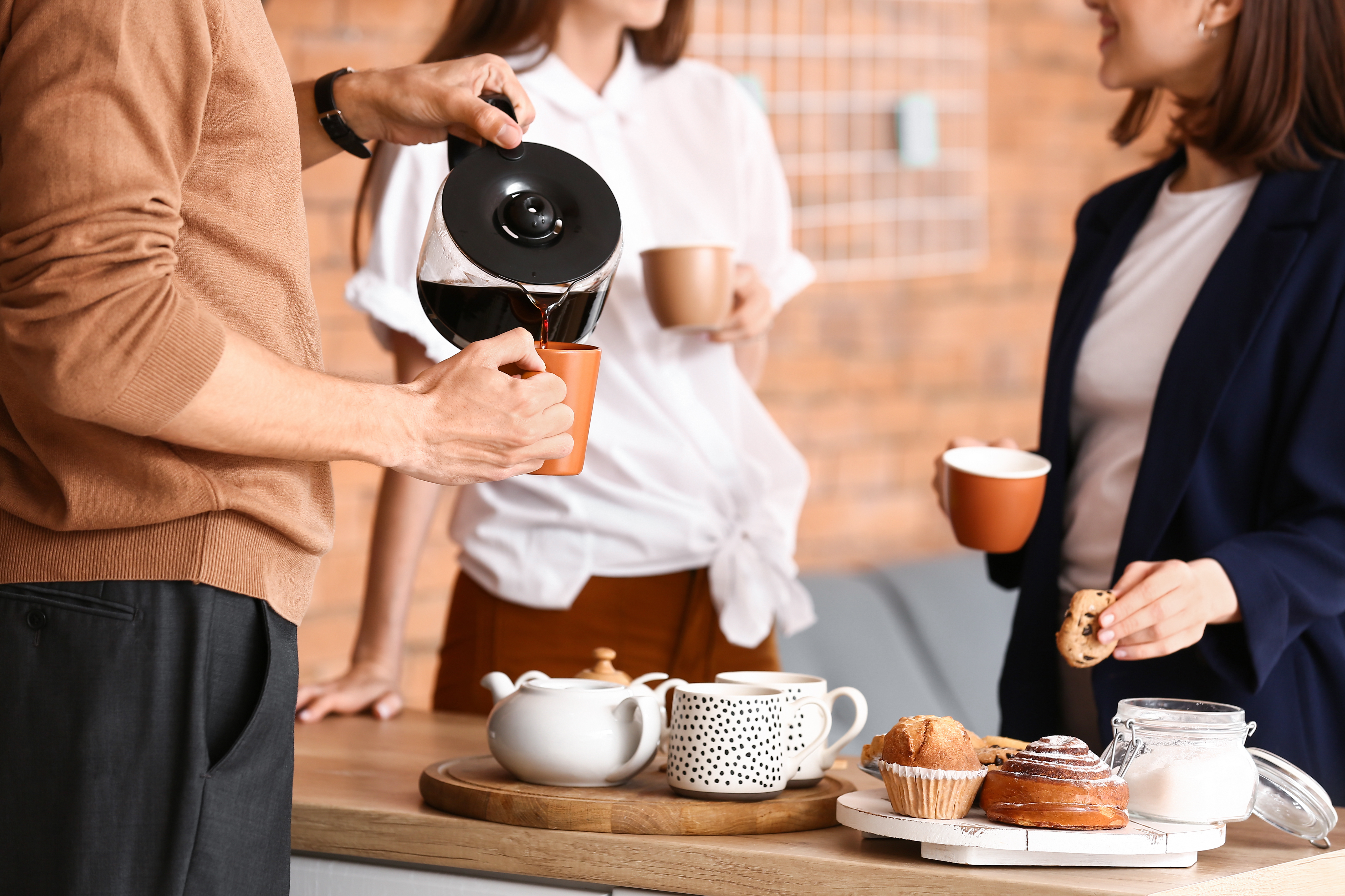 Three people dressed in business casual talking over a table of coffee and cakes