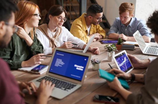 Group of diverse people working together on a large table with laptops