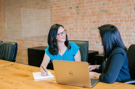 Two seated women chatting with a laptop open on a table.