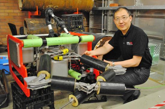 Distinguished Professor Dikai Liu kneels beside a robotic device.