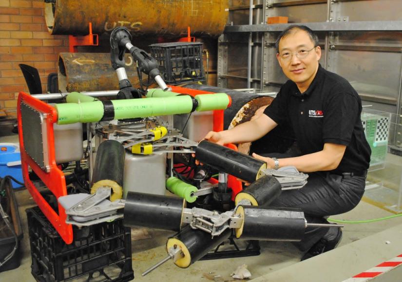 Distinguished Professor Dikai Liu kneels beside a robotic device.